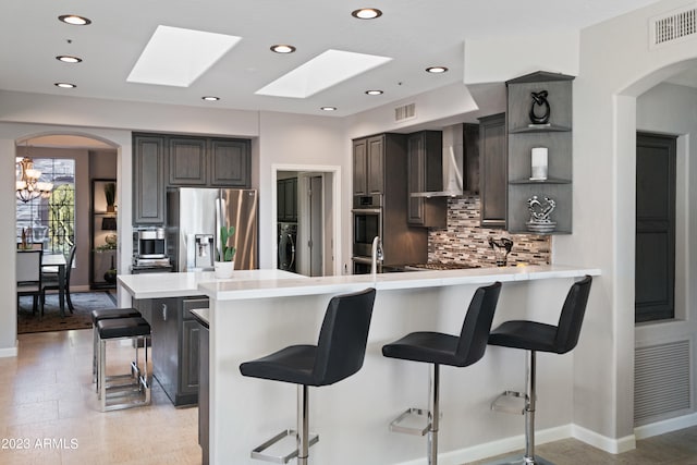 kitchen featuring wall chimney range hood, a breakfast bar, appliances with stainless steel finishes, tasteful backsplash, and washer / dryer