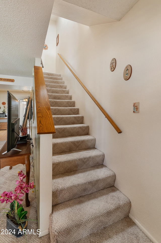 stairway featuring carpet flooring and a textured ceiling