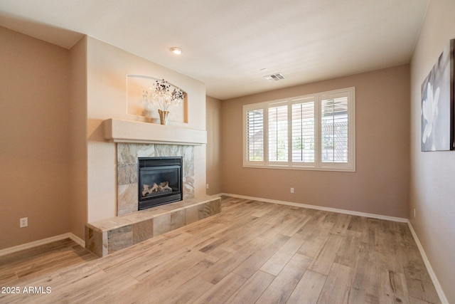 unfurnished living room with baseboards, visible vents, a tile fireplace, and wood finished floors