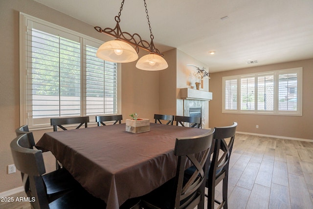 dining area with a tiled fireplace, baseboards, wood finished floors, and visible vents