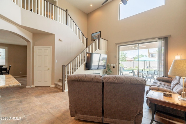 living room featuring arched walkways, stairs, a ceiling fan, and a towering ceiling