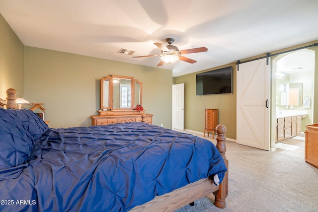 bedroom featuring connected bathroom, a barn door, light carpet, a ceiling fan, and visible vents