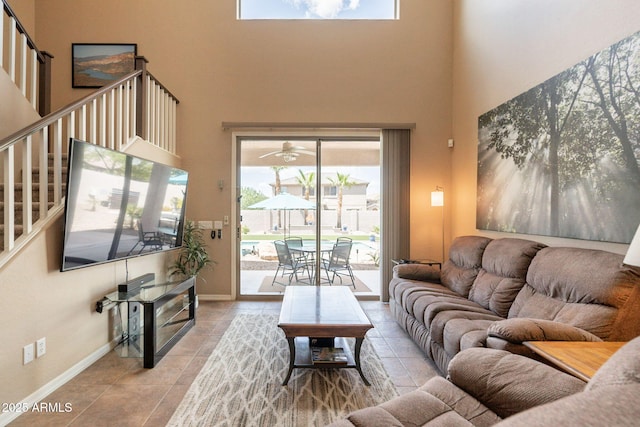 tiled living room with baseboards, a ceiling fan, stairs, and a towering ceiling