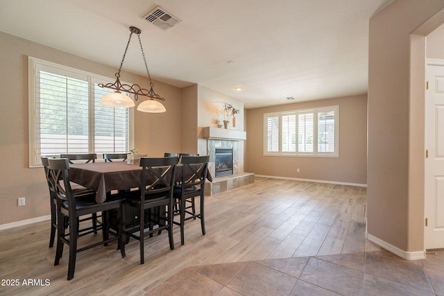 dining space with a tiled fireplace, baseboards, wood finished floors, and visible vents