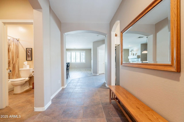 hallway with arched walkways, baseboards, and tile patterned floors