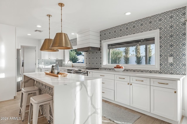 kitchen with light wood-type flooring, a kitchen island, light stone counters, white cabinetry, and stainless steel appliances