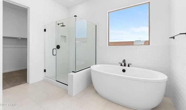 full bathroom featuring a stall shower, a spacious closet, a freestanding tub, and tile walls