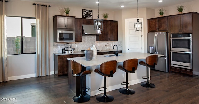 kitchen with under cabinet range hood, dark wood-type flooring, a sink, appliances with stainless steel finishes, and decorative backsplash