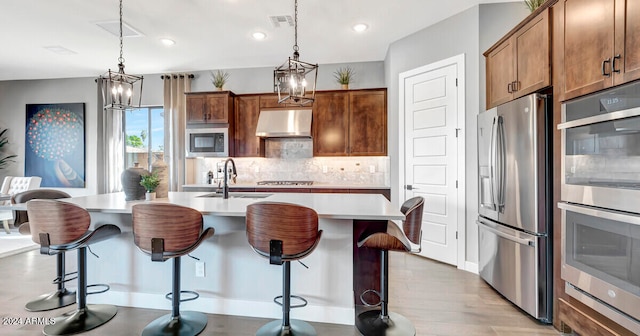 kitchen featuring hanging light fixtures, stainless steel appliances, a kitchen breakfast bar, light hardwood / wood-style flooring, and a center island with sink