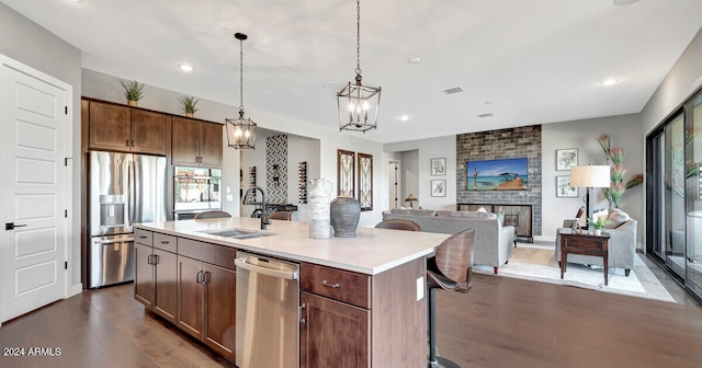 kitchen featuring a center island with sink, sink, a brick fireplace, dark hardwood / wood-style flooring, and stainless steel appliances