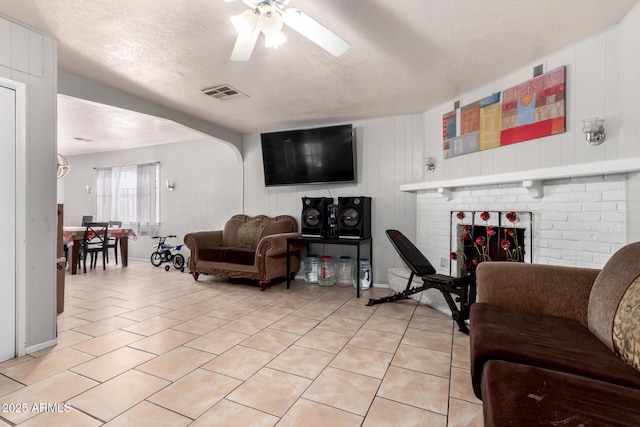 living room with ceiling fan, a brick fireplace, a textured ceiling, and light tile patterned floors