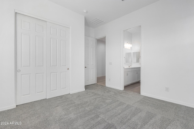 unfurnished bedroom with light carpet, a closet, and ensuite bath