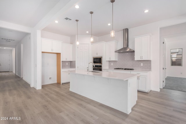 kitchen with white cabinetry, wall chimney exhaust hood, light hardwood / wood-style flooring, and an island with sink