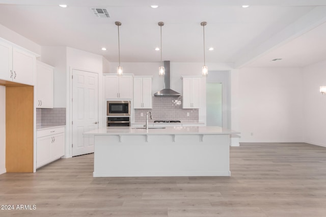 kitchen with appliances with stainless steel finishes, wall chimney exhaust hood, white cabinetry, and light wood-type flooring