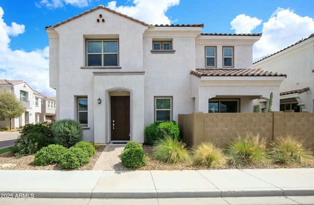 mediterranean / spanish house featuring a tile roof, fence, and stucco siding