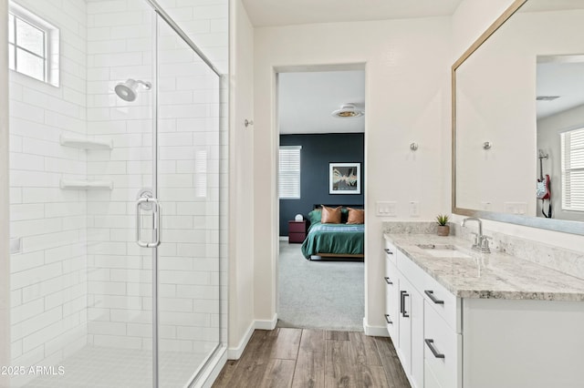 ensuite bathroom with a stall shower, wood finished floors, ensuite bath, baseboards, and vanity