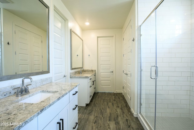 full bath featuring a sink, wood finished floors, two vanities, and a stall shower