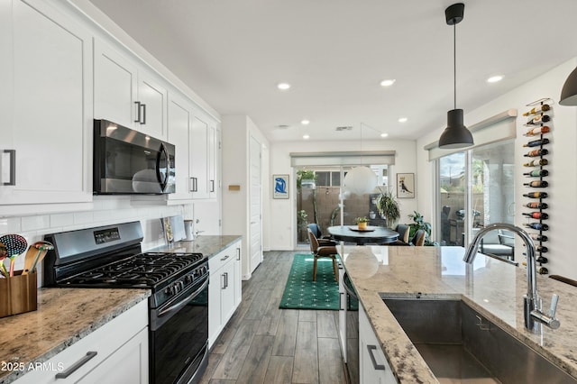 kitchen with wood finished floors, a sink, appliances with stainless steel finishes, white cabinetry, and tasteful backsplash