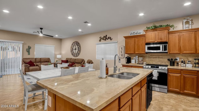 kitchen featuring brown cabinetry, an island with sink, open floor plan, stainless steel appliances, and a sink