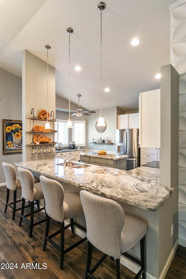 kitchen with dark hardwood / wood-style flooring, a kitchen breakfast bar, kitchen peninsula, and stainless steel fridge