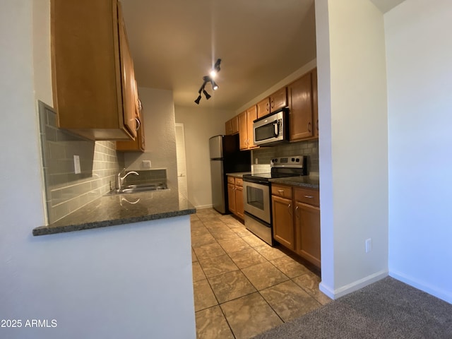 kitchen featuring light tile patterned floors, a sink, baseboards, appliances with stainless steel finishes, and decorative backsplash