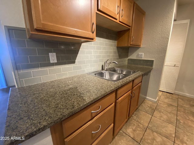 kitchen featuring light tile patterned floors, backsplash, brown cabinetry, a sink, and baseboards