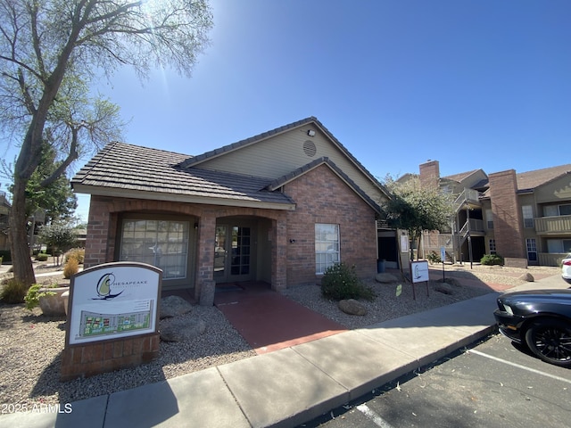 view of front of house with uncovered parking, brick siding, and a tile roof