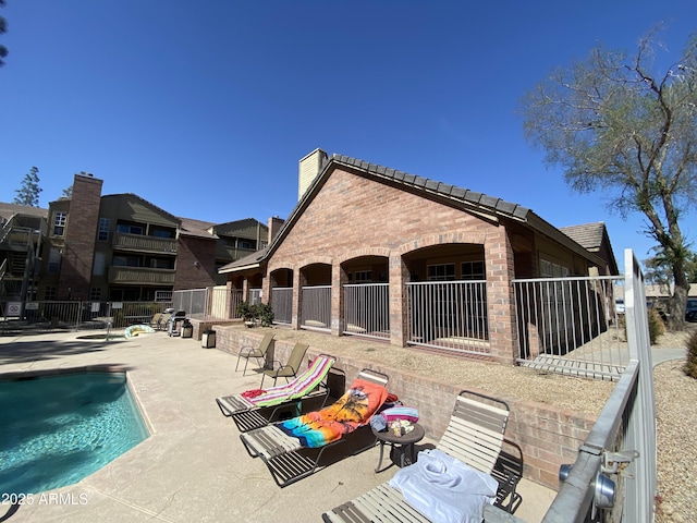 exterior space featuring a community pool, brick siding, a tile roof, fence, and a patio area