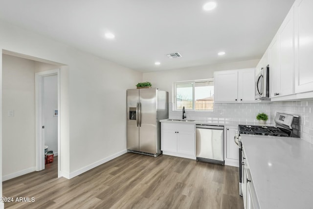 kitchen featuring stainless steel appliances, decorative backsplash, white cabinets, light hardwood / wood-style flooring, and sink