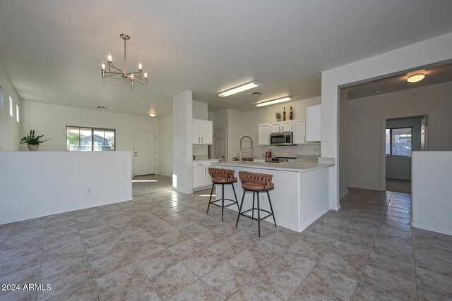 kitchen featuring white cabinetry, sink, pendant lighting, a chandelier, and a kitchen bar