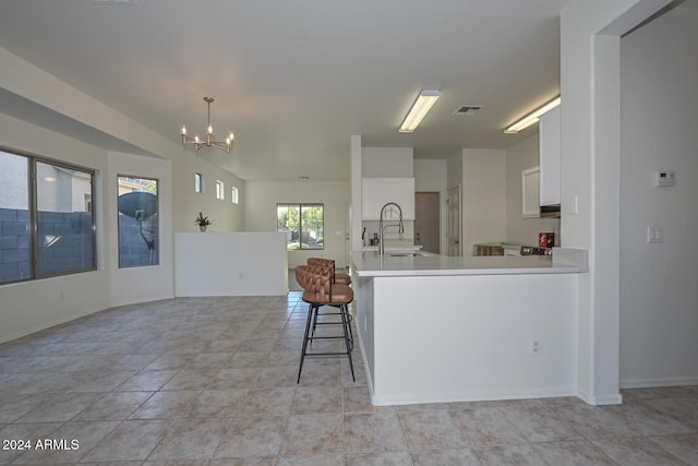 kitchen featuring sink, a chandelier, pendant lighting, a kitchen bar, and white cabinets