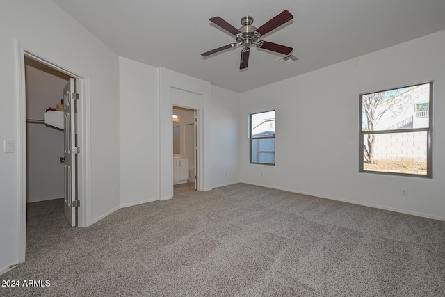 unfurnished bedroom with light colored carpet, a spacious closet, multiple windows, and ensuite bathroom