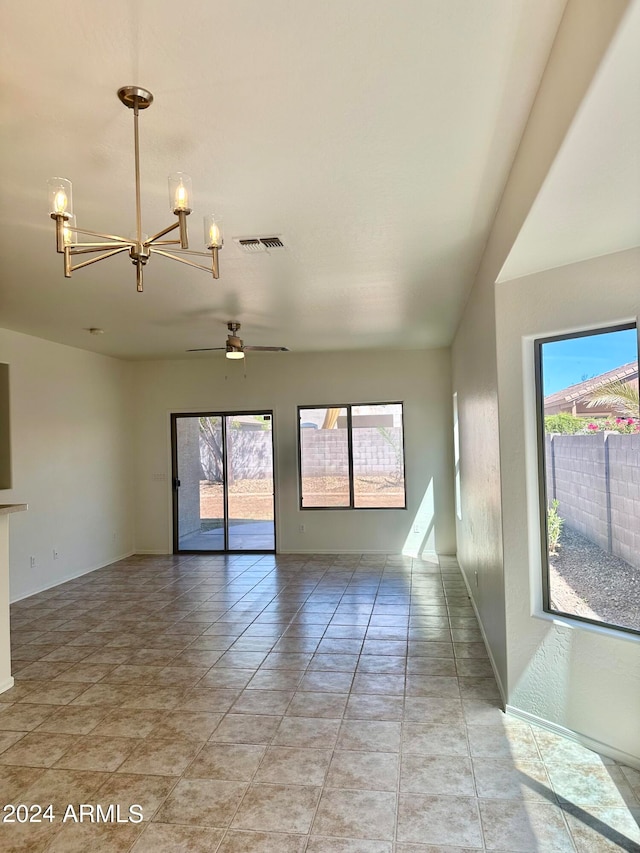 tiled empty room featuring plenty of natural light and ceiling fan with notable chandelier