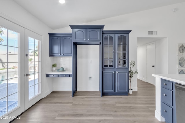 kitchen with glass insert cabinets, vaulted ceiling, light countertops, french doors, and stainless steel dishwasher