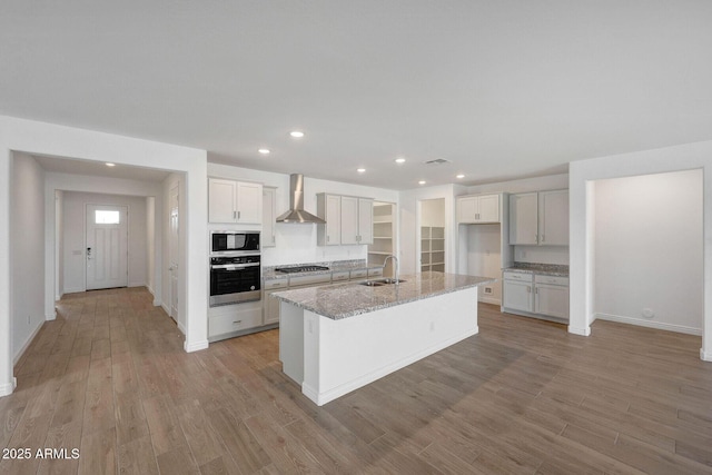 14789 W Lariat Ln, Surprise, AZ 85387 - kitchen with appliances with stainless steel finishes, a sink, wall chimney range hood, light wood-style flooring, and baseboards