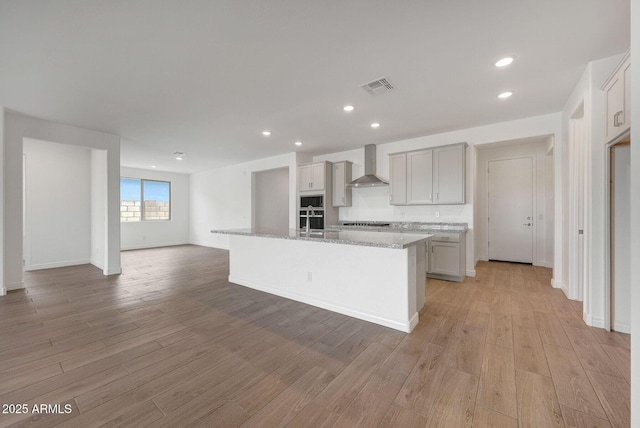 14789 W Lariat Ln, Surprise, AZ 85387 - kitchen with wall chimney exhaust hood, open floor plan, light wood-style flooring, a kitchen island with sink, and recessed lighting