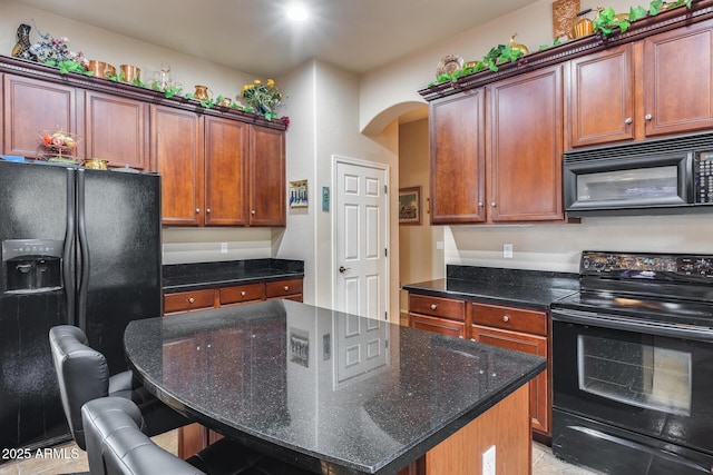 kitchen with dark stone countertops, black appliances, a breakfast bar, and a kitchen island