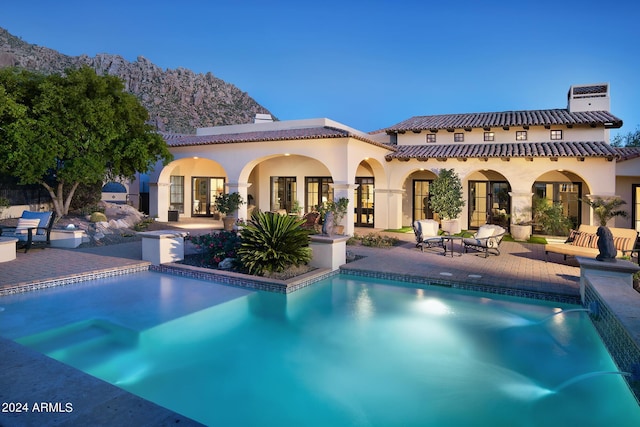 back house at dusk with pool water feature, a patio area, and french doors