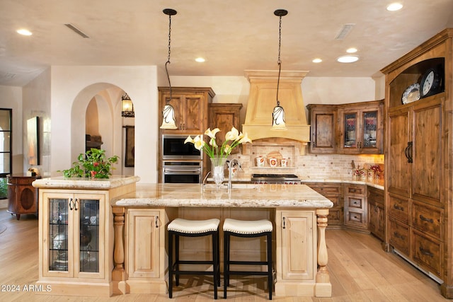 kitchen with appliances with stainless steel finishes, a kitchen breakfast bar, a kitchen island with sink, light hardwood / wood-style floors, and hanging light fixtures