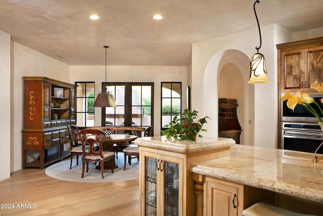 kitchen with hanging light fixtures, light wood-type flooring, beverage cooler, and light stone countertops