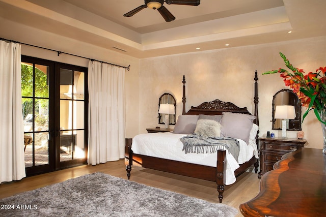 bedroom with access to exterior, french doors, light wood-type flooring, a raised ceiling, and ceiling fan