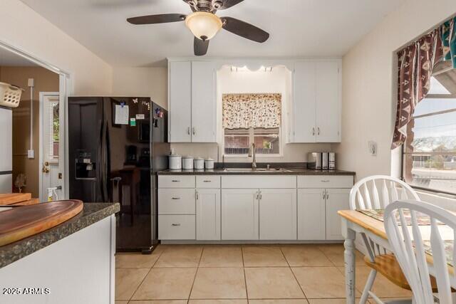 kitchen featuring dark countertops, a sink, a ceiling fan, light tile patterned flooring, and black fridge