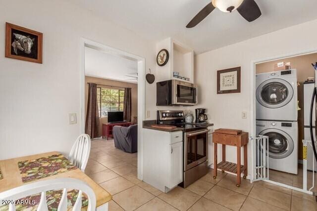 kitchen with stacked washer / drying machine, stainless steel appliances, light tile patterned floors, dark countertops, and a ceiling fan