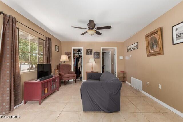 living area with light tile patterned floors, visible vents, a ceiling fan, and baseboards
