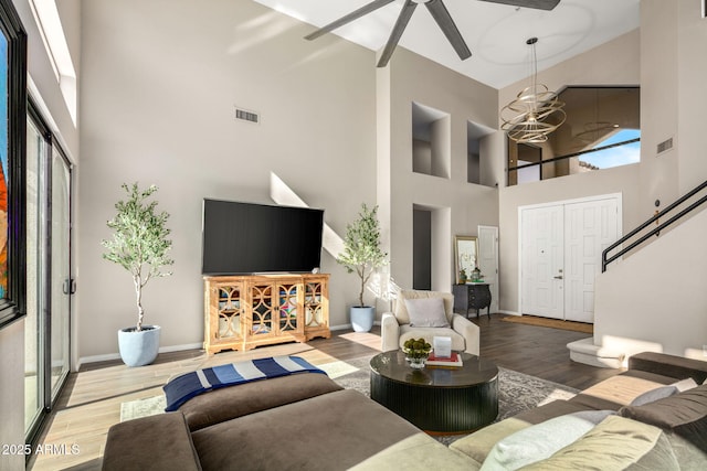 living room with ceiling fan with notable chandelier, wood-type flooring, and a towering ceiling