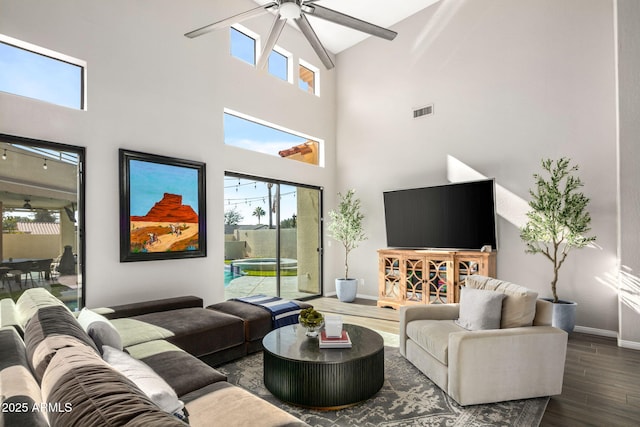 living room featuring dark wood-type flooring, ceiling fan, and a towering ceiling