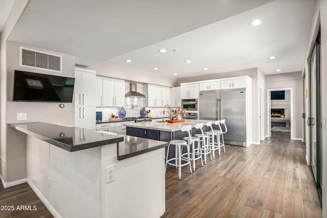 kitchen featuring a kitchen bar, dark hardwood / wood-style flooring, white cabinets, stainless steel appliances, and wall chimney range hood