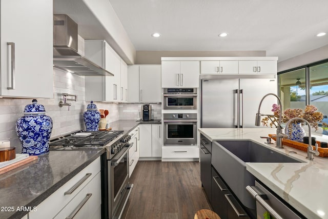 kitchen featuring white cabinets, dark hardwood / wood-style flooring, light stone counters, stainless steel appliances, and wall chimney exhaust hood