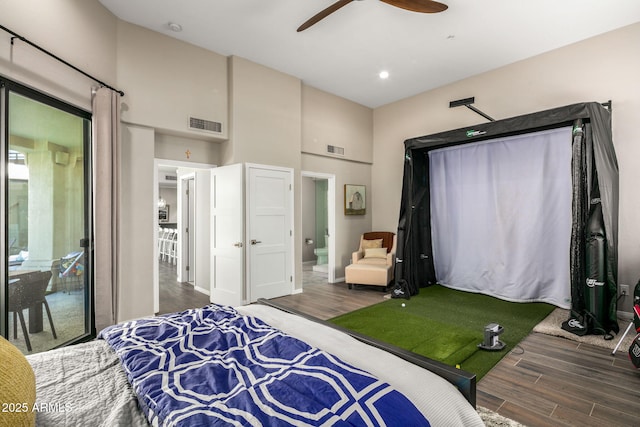 bedroom with ceiling fan, golf simulator, connected bathroom, and dark hardwood / wood-style flooring