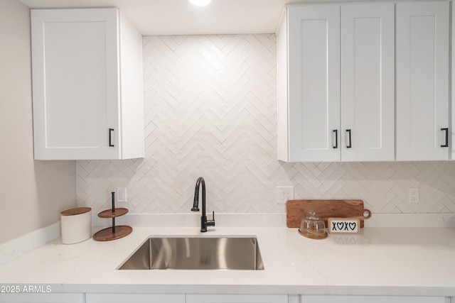 kitchen featuring sink, decorative backsplash, light stone countertops, and white cabinets